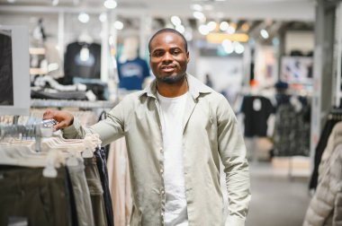 Şık bir Afro-Amerikan erkeği perakende mağazasında yeni kıyafetler seçiyor, alışveriş deneyiminin keyfini çıkarıyor.