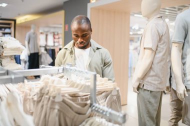 Odaklanmış Afro-Amerikalı adam giyim mağazasında yeni pantolon seçiyor, alışverişin tadını çıkarıyor ve satın alma kararı veriyor.