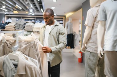 Şık bir Afro-Amerikan erkeği bir giyim mağazasında pantolon seçiyor, yeni moda trendlerini keşfediyor.
