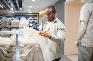 Mutlu müşteri elbise rafından gömlek seçiyor, perakende mağazasında alışveriş deneyiminin tadını çıkarıyor.