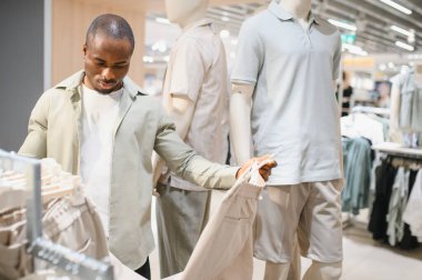 Şık bir Afro-Amerikan erkeği giyim mağazasında pantolon seçiyor, alışveriş deneyiminin tadını çıkarıyor.