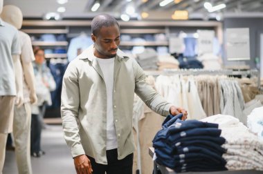 Alışveriş merkezinde kıyafet seçen bir adam stile ve modaya odaklanıyor. Değişik kıyafetleri inceliyor, modaya uygun seçimler yaparak gardırobunu geliştiriyor.