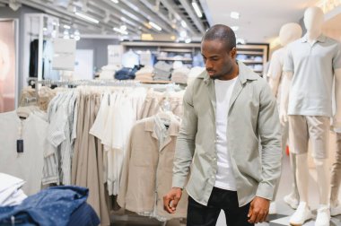 Genç, şık, Afro-Amerikalı bir adam moda mağazasından kıyafet seçiyor. Perakende mağazasından kıyafet seçmeye odaklanıyor.