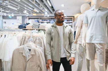 Modern bir alışveriş merkezinde kıyafet seçen şık bir Afro-Amerikan erkeği alışveriş deneyiminin tadını çıkarıyor.