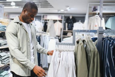 Afro-Amerikalı bir adam alışveriş merkezinde kıyafet seçeneklerini araştırıyor. Moda ve stile odaklanıyor ve mükemmel kıyafeti seçiyor.