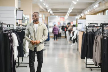 Müşteri giyim mağazası koridorlarında yürüyor, şık yeni kıyafetler arıyor ve çeşitli moda giyim seçeneklerini inceliyor.