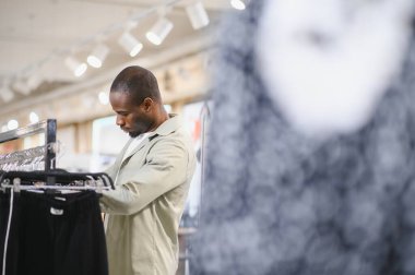 Şık bir Afro-Amerikan erkeği giyim mağazasında elbise seçerken, alışveriş deneyiminin tadını çıkarıyor.