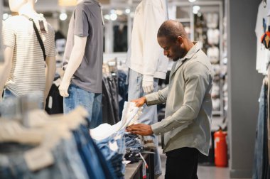 Şık bir adam giyim mağazasında geziniyor, kaliteli ve uygun kot pantolon için titizlikle inceliyor ve mükemmel kot pantolon seçiyor.