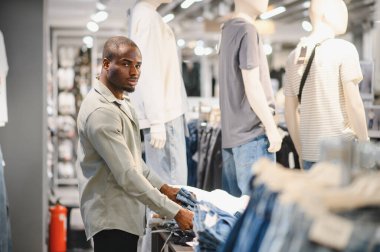 Müşteri şık bir kot pantolon seçerken, modern bir giyim mağazasına göz gezdiriyor, çeşitli modaya uygun giyim ürünleri sergiliyor.