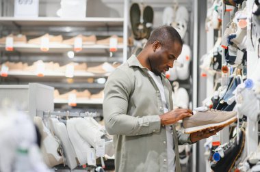 Modern bir ayakkabı mağazasında alışveriş yaparken bir çift spor ayakkabısını dikkatle inceleyen Afrikalı Amerikalı bir adam,