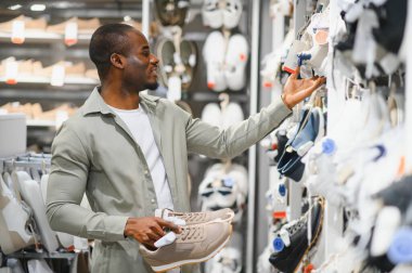 Afro-amerikan erkek alışveriş merkezinde alışveriş yapıyor, şık spor ayakkabıları seçiyor, moda anlayışını ve modern tüketici alışkanlıklarını sergiliyor.