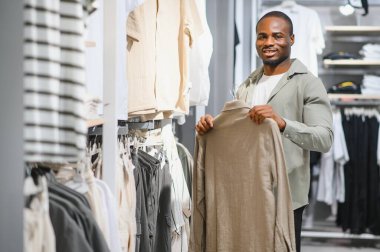 Afro-amerikan bir adam alışveriş merkezinde alışveriş gününün tadını çıkarıyor, şık kıyafetler seçiyor, kişisel tarzını gözler önüne seriyor.