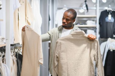 Bir perakende mağazasında kıyafet alırken iki gömleği karşılaştıran müşteri, stil ve tercihlerine göre satın alma kararları alıyor