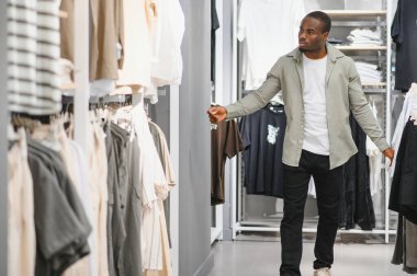 Müşteri canlı bir perakende mağazasında elbise raflarını karıştırıyor, çeşitli stilleri düşünceli bir şekilde düşünüyor ve satın alma kararları alıyor.