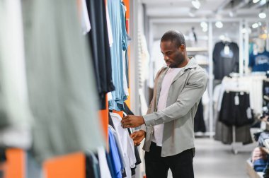 Afro-Amerikalı bir adam moda bir alışveriş merkezinde kıyafet seçeneklerini araştırıyor, moda ve modaya odaklanıyor.