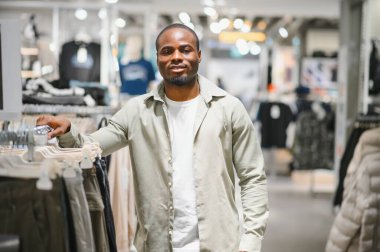 Modern bir alışveriş merkezinde moda seçeneklerini araştıran Afro-Amerikalı bir adam stil ve kıyafet seçimlerine özgüven ve şevkle odaklanıyor.