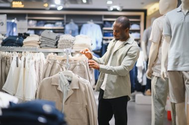 Modern bir giyim mağazasında elbise seçen şık bir Afro-Amerikan erkeği alışveriş deneyiminin tadını çıkarıyor.