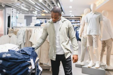 Şık bir adam giyim mağazasında yeni gömlek seçiyor, alışveriş deneyiminden ve modern moda eğilimlerinden zevk alıyor