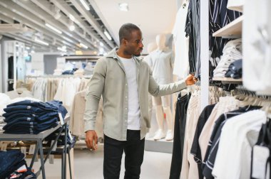 Giysi mağazasında gömlek seçen şık bir adam, alışveriş deneyiminden zevk alıyor ve yeni koleksiyon yapıyor.