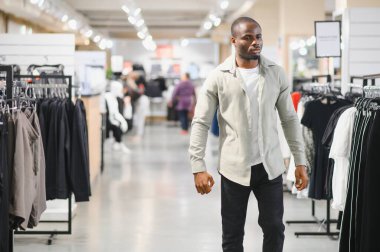 Müşteri alışveriş merkezinde elbise raflarında yürüyor, hafta sonu alışveriş deneyiminin tadını çıkarıyor.