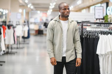 Perakende mağazasında kıyafet seçen şık bir adam, parlak ve modern bir alışveriş merkezinde alışveriş deneyiminin tadını çıkarıyor.