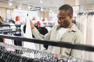 Afro-Amerikalı bir adam beyaz bir gömlek seçiyor, alışveriş deneyiminin tadını çıkarıyor.