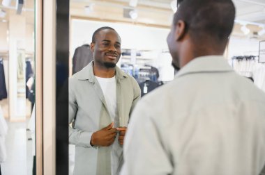 Mutlu Afro-Amerikalı adam giyinme odasındaki aynadaki yansımasına bakarken kıyafetlerini düzeltiyor.