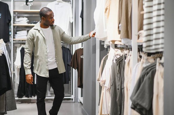 Клиент просматривает стойки одежды, выбирает рубашку в современном розничном магазине, наслаждается покупками
