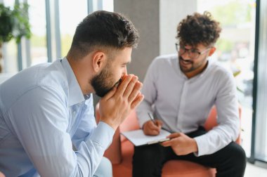 Psikolog, ofiste terapi seansında erkek hastasının sorunlarını anlatırken not alıyor.