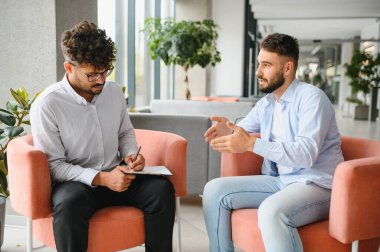 Erkek hasta sorunlarını modern ofiste terapi seansında not alan psikologlara anlatıyor.