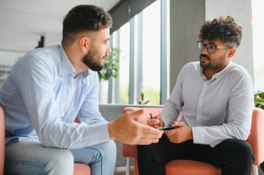 Psikolog, modern ofiste terapi seansı sırasında erkek hastaların sorunlarını dinlerken not alıyor.