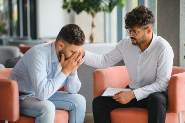 Özel terapi seansında acı çeken bir hastayı destekleyen erkek psikolog rehberlik ve empati sunuyor.