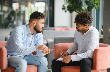 Psikolog terapi seansı sırasında erkek hastaların sorunlarını anlatırken not alıyor.