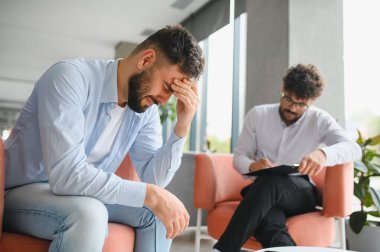 Psikolog, depresyon geçiren bir erkek hastayla terapi seansında notlar alıyor. İyileşmek için destekleyici bir ortam sağlıyor.