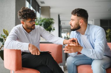 Erkek psikolog ellerini tutarak ve terapi seansında rahatlık ve empati sağlayarak hastasını destekliyor.