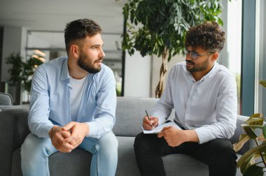 Psikolog, modern ofiste terapi seansı sırasında erkek hastaların sorunları hakkında konuşmalarını dinlerken not alıyor.