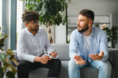 Erkek hasta sorunlarını modern ofiste terapi seansı sırasında not alan psikologlara anlatıyor.