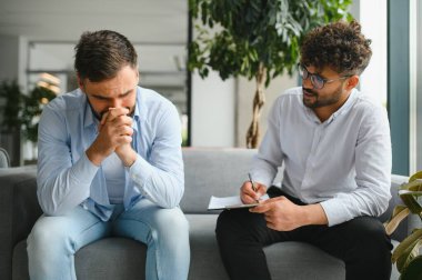 Psikolog, psikolojik sorunları olan bir erkek hastayla terapi seansı sırasında not alıyor.