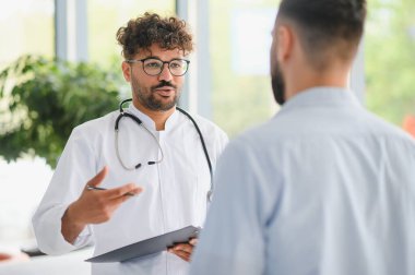 Doktor elinde bir dosya tutarak hastaya tanıyı açıklıyor. Parlak, modern bir özel klinikte, iletişimi ve güveni destekliyor.