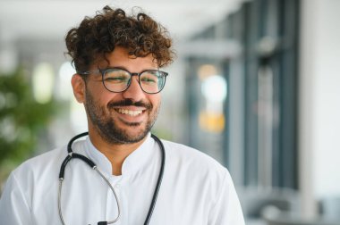 Dost canlısı Arap doktor klinikte gülümsüyor, gözlük ve steteskop takıyor, sağlık hizmeti kavramı