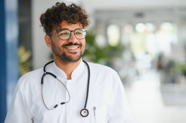 Hastane koridorunda gülümseyen dost canlısı Arap doktor, sağlık hizmetlerinde sağlık, çeşitlilik ve profesyonelliği temsil ediyor.