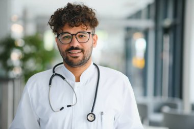 Modern klinikte gülümseyen kendine güvenen erkek doktor, sağlık ve tıbbi uzmanlığı temsil ediyor.