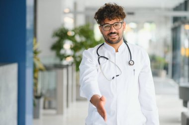 Gülümseyen Arap doktor el sıkışmak için elini uzatıyor. Parlak, modern tıp kliniğinde hastaları ağırlıyor.