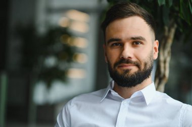 Beyaz gömlek giyen, modern bir ofis alanında kurumsal bir vesikalık fotoğraf için poz veren sakallı girişimci.