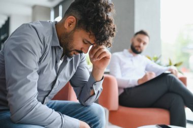 Travma sonrası stres bozukluğundan muzdarip bir adam ofisinde bir psikologla terapi seansı yapıyor.