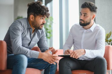 Üzgün bir Arap adam, modern bir ofis ortamında terapi seansında notlar alan psikologla kişisel sorunları tartışıyor.