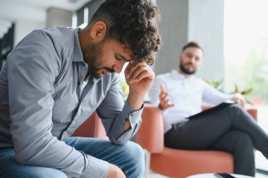 Terapi seansı sırasında travma sonrası stres bozukluğu yaşayan Arap bir adam ofis ortamında bir psikologla duygu ve zorlukları tartışıyor.