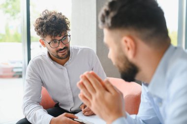 Psikolog terapi seansı sırasında erkek hastaların sorunlarını dinlerken not alıyor.