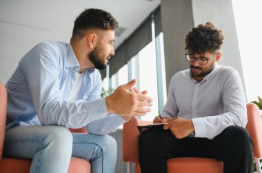 Psikolog terapi seansında erkek bir hastayla sorunlarını tartışırken not alıyor.