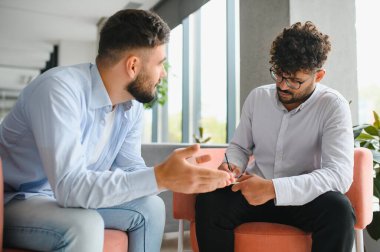 Erkek hasta sorunlarından bahsediyor ve psikolog ofisteki terapi seansında not alıyor.